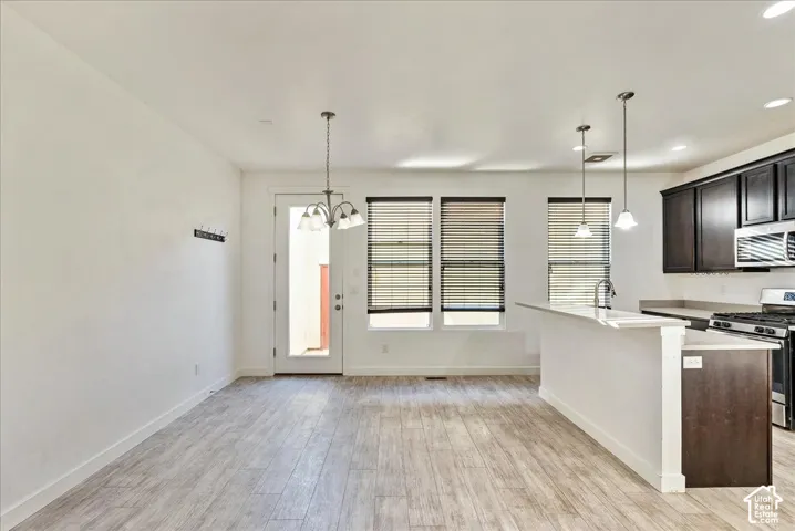 Open-concept living space featuring wood-finish flooring, a kitchen island with seating, dark wood cabinetry, stainless steel appliances, and multiple windows with blinds