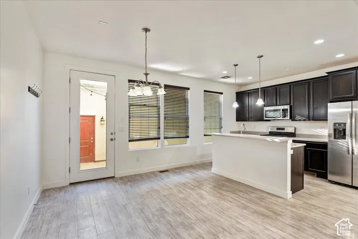 Open-concept living area with wood-finish flooring, a kitchen island, dark wood cabinetry, and stainless steel appliances