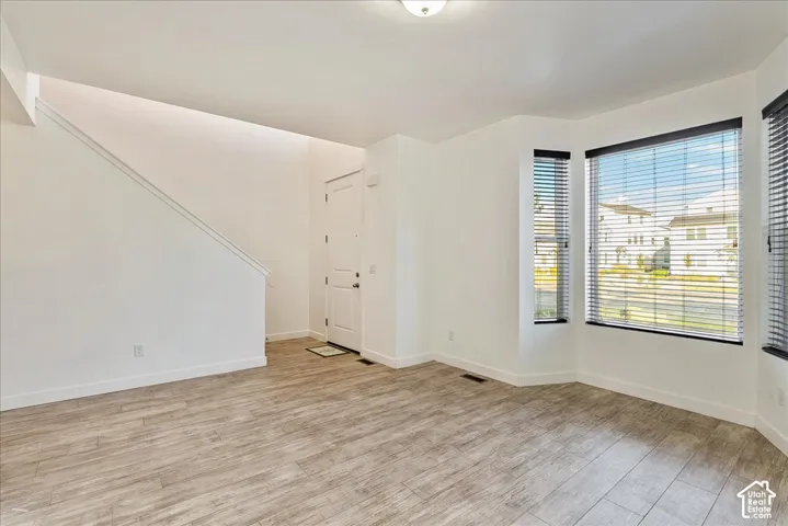 Spacious living area featuring wood-finish flooring, a bay window with blinds, and white walls