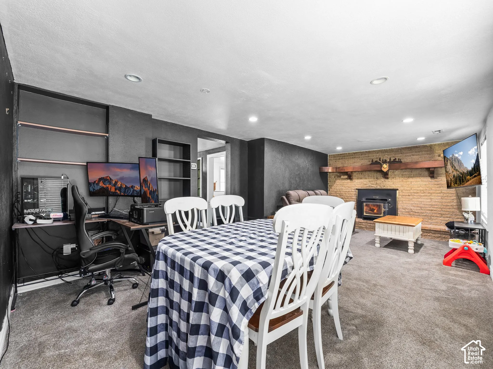 Recessed ceiling lighting, carpeted flooring, brick-faced wall with wood mantel, and wood-burning stove