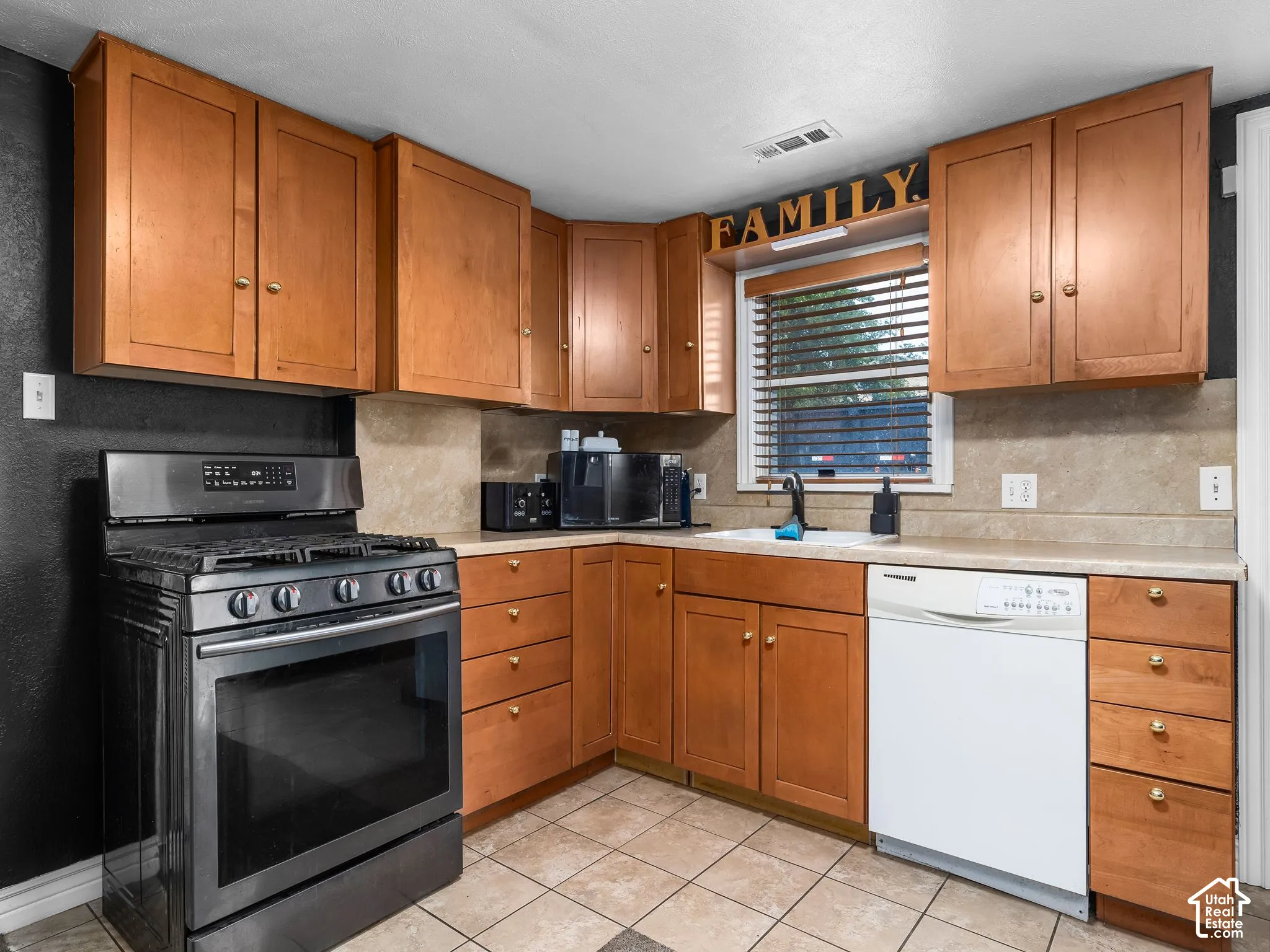 U-shaped kitchen featuring wood cabinetry, stainless steel range, white dishwasher, and a tile backsplash