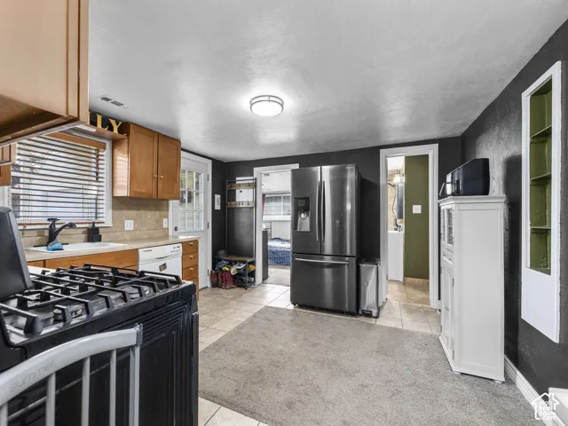 Kitchen featuring wood cabinetry, a gas range, a double-basin sink, and tile flooring