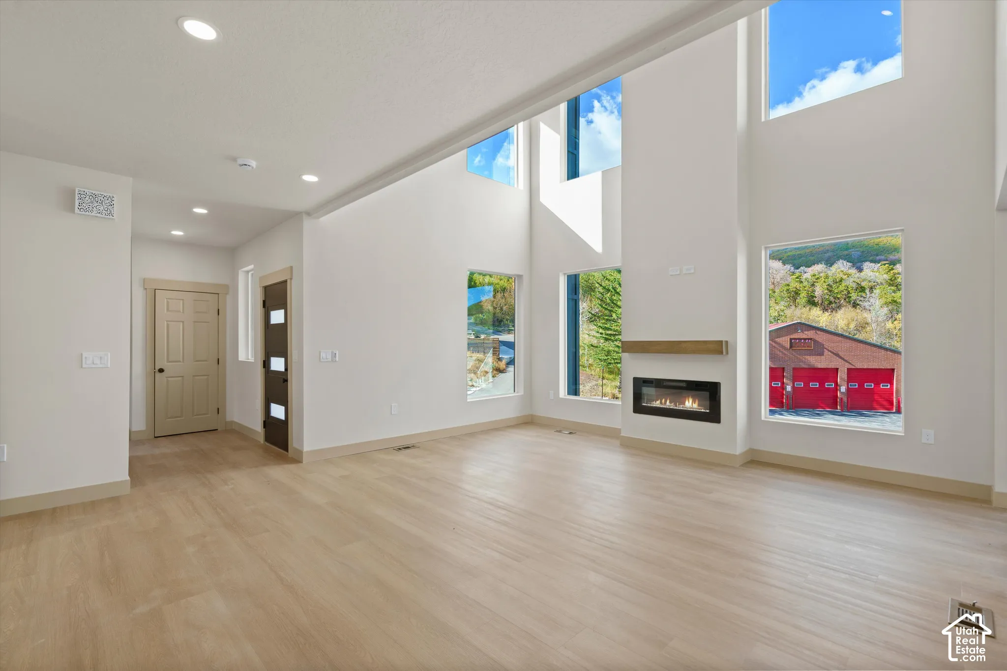 Vaulted ceilings with large windows, an integrated fireplace with a wood mantel, and wood-finish flooring