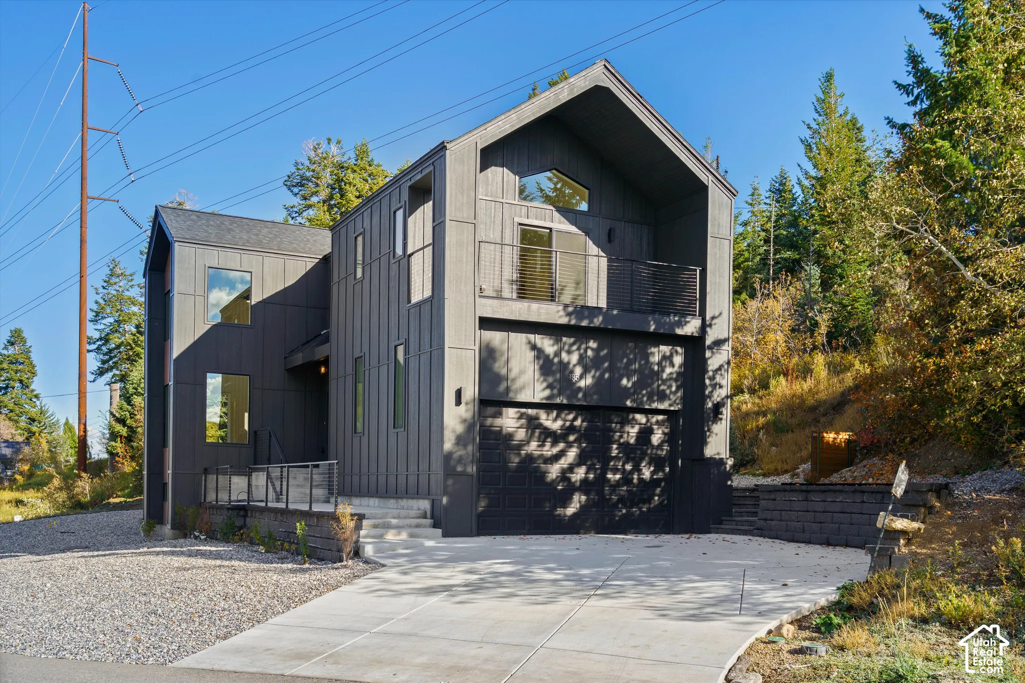 Modern architectural exterior featuring vertical siding, a pitched roofline, multiple windows, a second-story balcony with metal railings, and an attached two-car garage