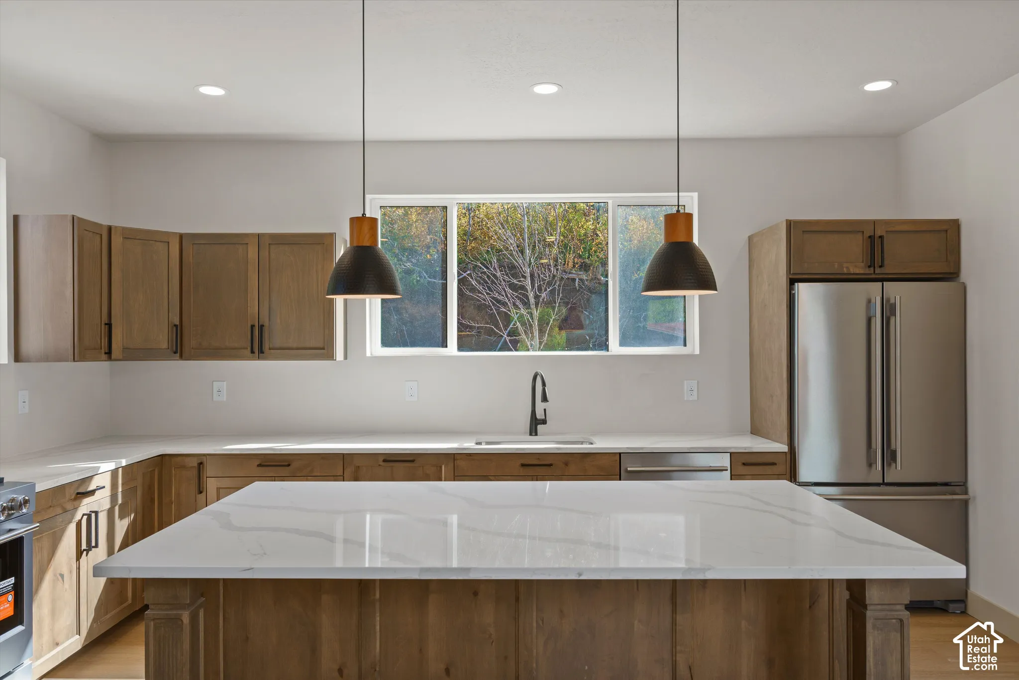 Kitchen featuring wood-finish cabinetry, stainless steel appliances, a large center island with a light-toned countertop, and recessed lighting