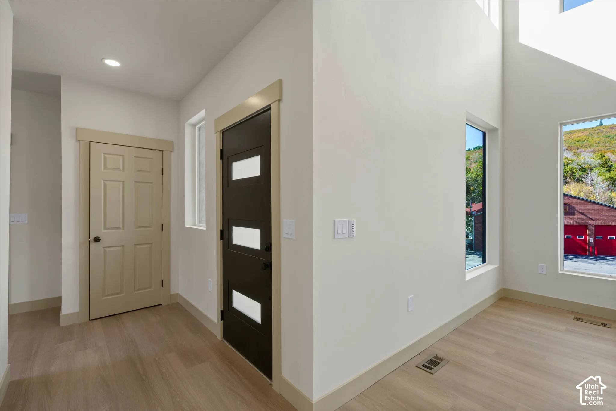 Wood-finish flooring throughout, modern entry door with frosted glass panels, recessed ceiling lighting, and large windows with integrated trim