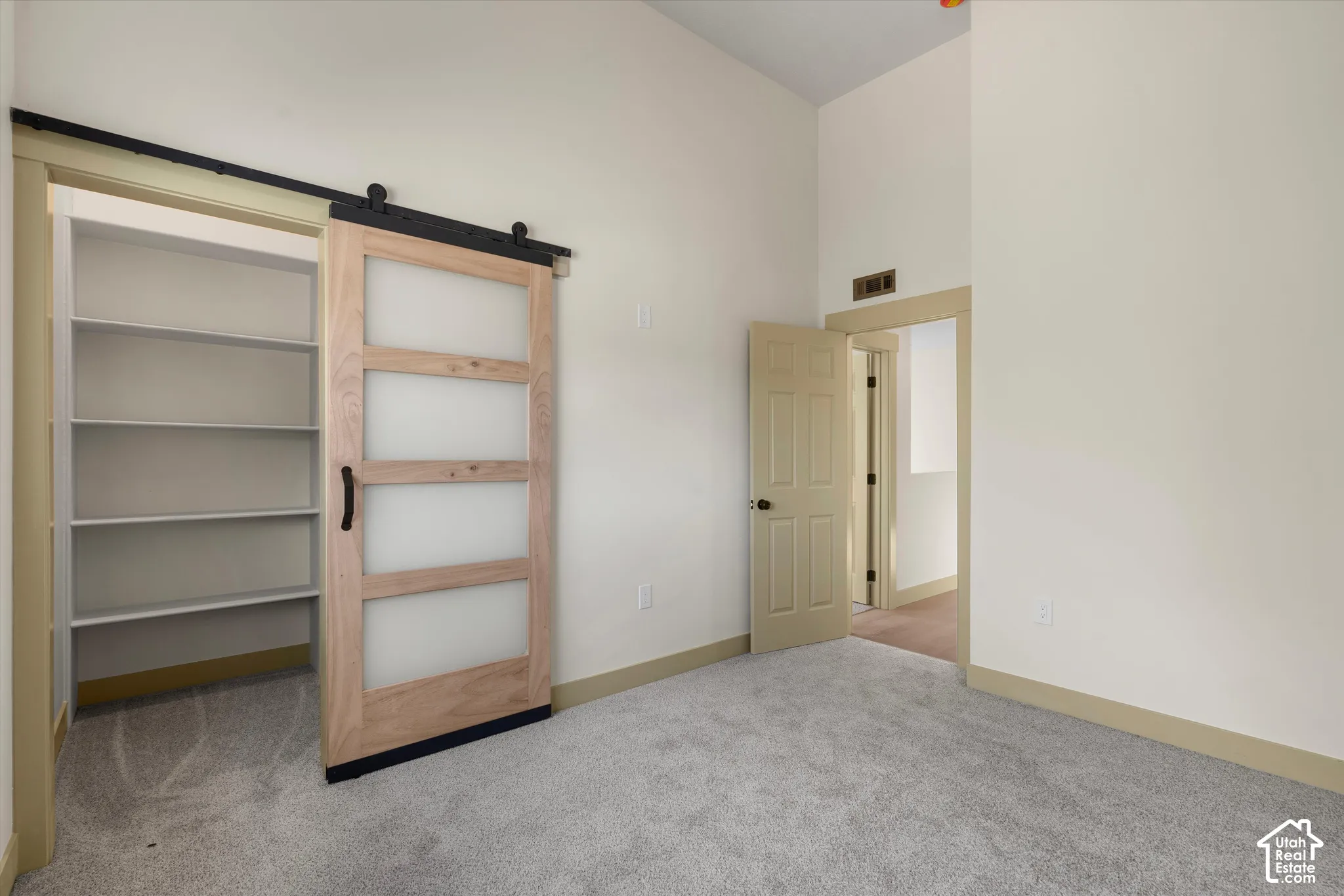 Sliding barn door with frosted glass panels, built-in shelving, vaulted ceiling, neutral wall tones, and plush carpeting