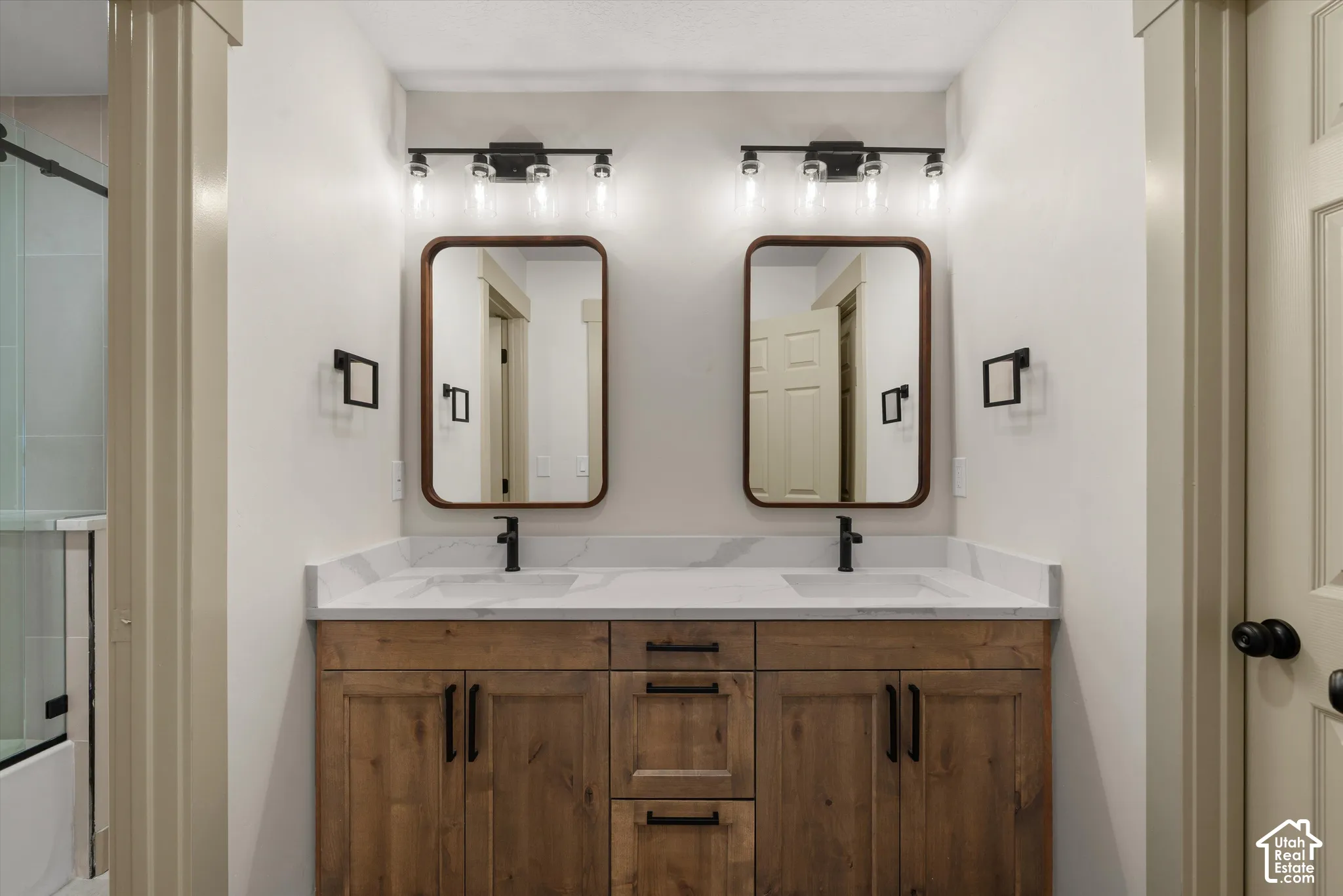 Dual vanity with wood-finish cabinetry, white countertop, rectangular undermount sinks, matte black faucets, and rectangular framed mirrors