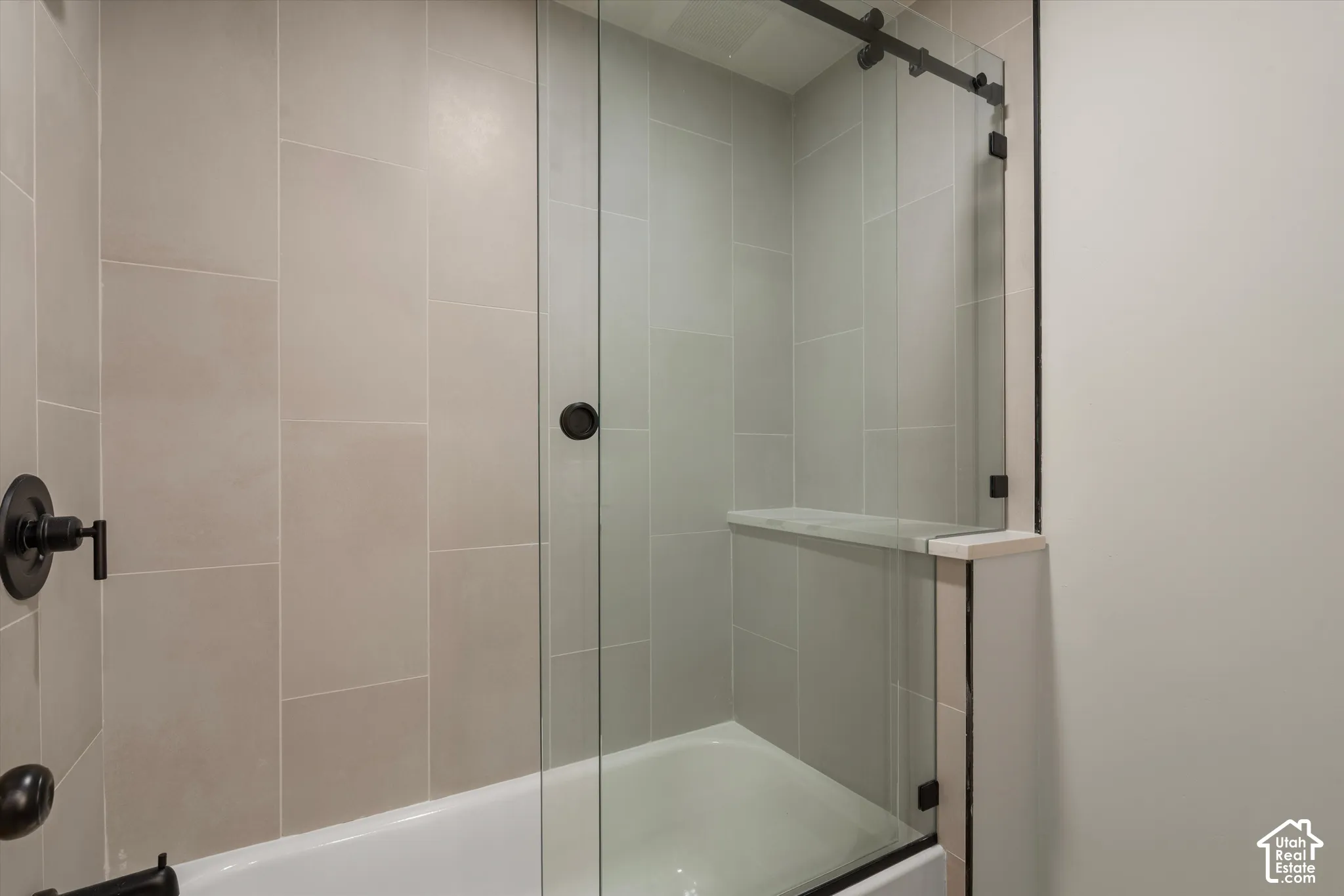 Guest Bathtub with sliding glass shower doors, matte black fixtures, and a built-in shower niche
