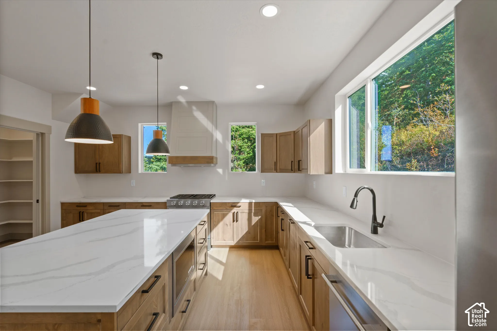 Kitchen featuring a large central island with a white countertop, wood-finish cabinetry, stainless steel sink with a matte black faucet, and recessed lighting