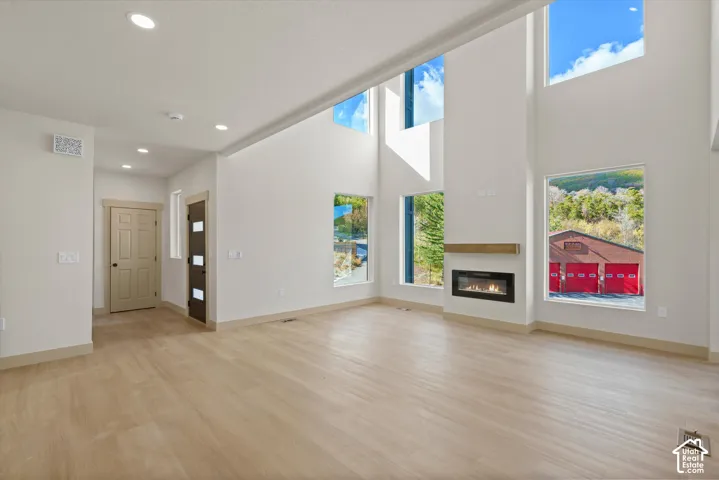 Vaulted ceilings with large windows, an integrated fireplace with a wood mantel, and wood-finish flooring