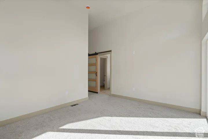 Primary Bedroom. Vaulted ceiling, light neutral wall paint, light-colored carpeting, modern barn door, and a recessed ceiling light
