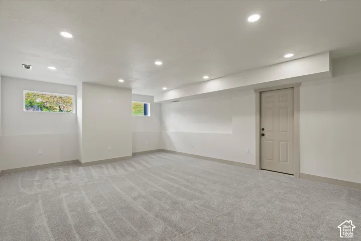Expansive room featuring recessed lighting, light-toned carpeting, two windows, and a paneled door
