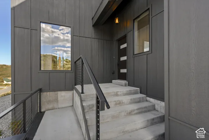 Front door. Modern exterior siding with vertical paneling, concrete steps, a contemporary entry door with frosted glass inserts, and sleek cable railings