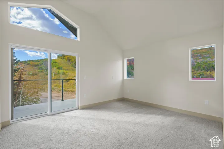 Primary bedroom. Vaulted ceilings with a high triangular window, sliding glass doors to the exterior, light-colored carpeting, and neutral wall tones