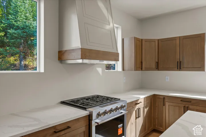 Stainless steel range, custom range hood, wood-finish cabinetry, light-toned countertops, and dual windows