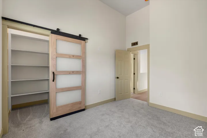Sliding barn door with frosted glass panels, built-in shelving, vaulted ceiling, neutral wall tones, and plush carpeting