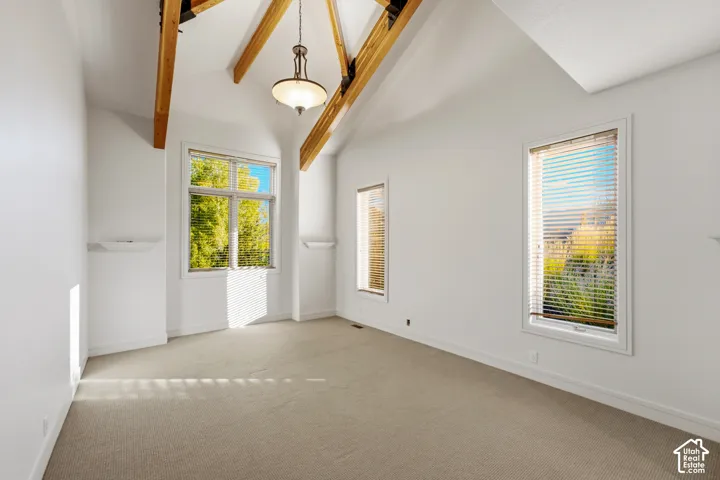 Vaulted ceiling with exposed wood beams, multiple windows, recessed wall shelving, and a central pendant light fixture