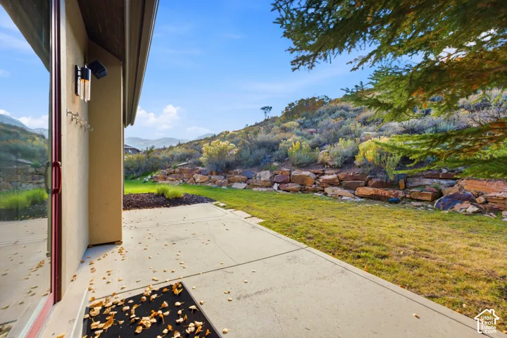 Concrete patio with a sliding glass door, exterior wall sconce, and a landscaped retaining wall