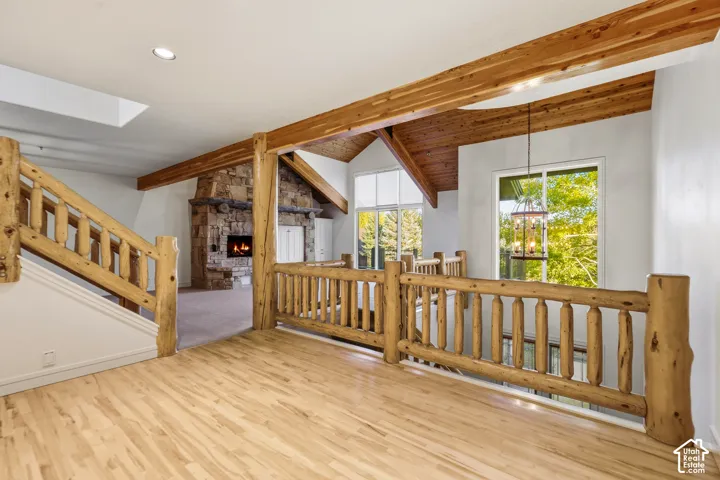 Wood-finish flooring, exposed wood beams, stone fireplace, vaulted wood-paneled ceiling, and large windows