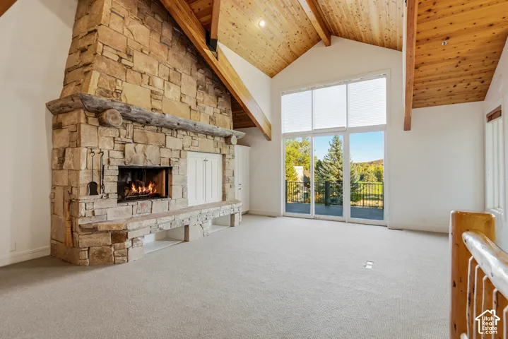 Vaulted wood-paneled ceiling with exposed beams, stone-clad fireplace with hearth, and full-height glass doors opening to an exterior balcony