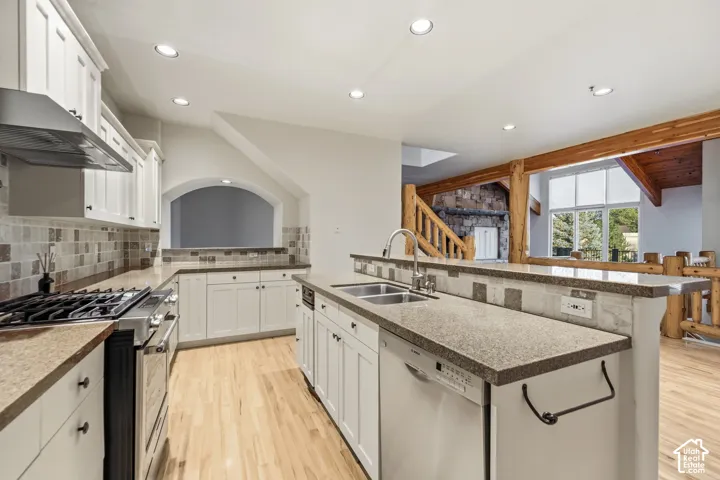 Kitchen featuring white cabinetry, stone-finish countertops, tile backsplash, stainless steel appliances, and a double basin sink
