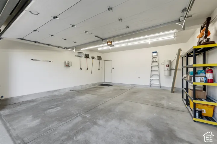 Attached garage with a concrete floor, built-in shelving, white walls, and overhead fluorescent lighting