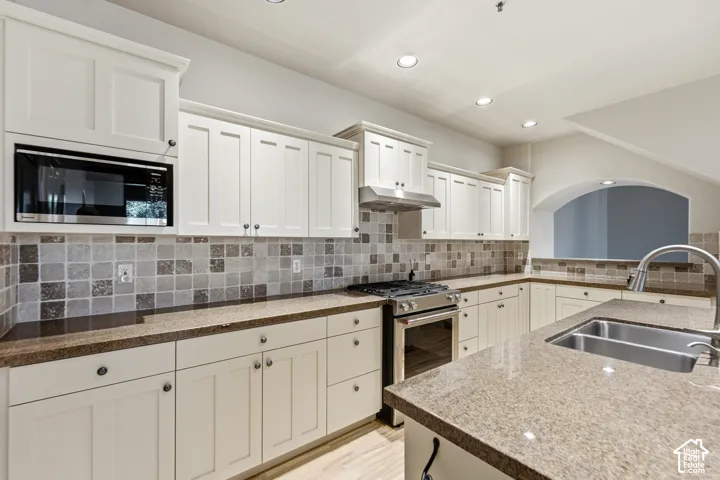 Kitchen featuring white shaker-style cabinetry, stainless steel appliances, speckled stone countertops, a mosaic tile backsplash, and recessed lighting