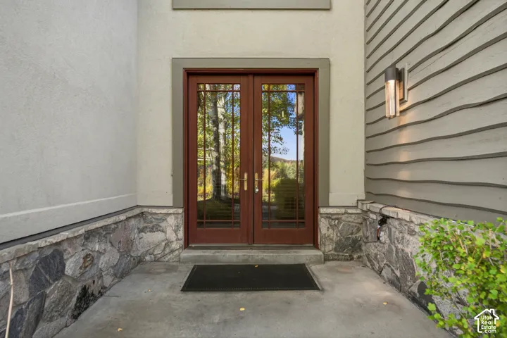 Double-door entry with divided lites, stone veneer detailing, stucco exterior, horizontal siding, and an exterior wall sconce