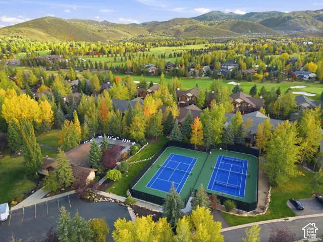 Two vibrant blue tennis courts, extensive tree coverage, surrounding golf course, mountain backdrop, and multiple residential structures