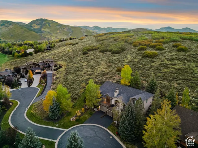 Hillside property featuring a multi-story residence with a dark shingle roof, paved driveway, and established trees