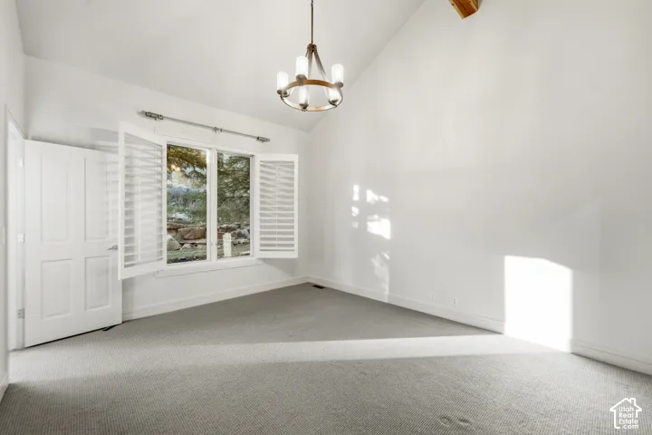Vaulted ceiling, ceiling-mounted light fixture, white interior doors, window with shutter blinds, and gray carpet