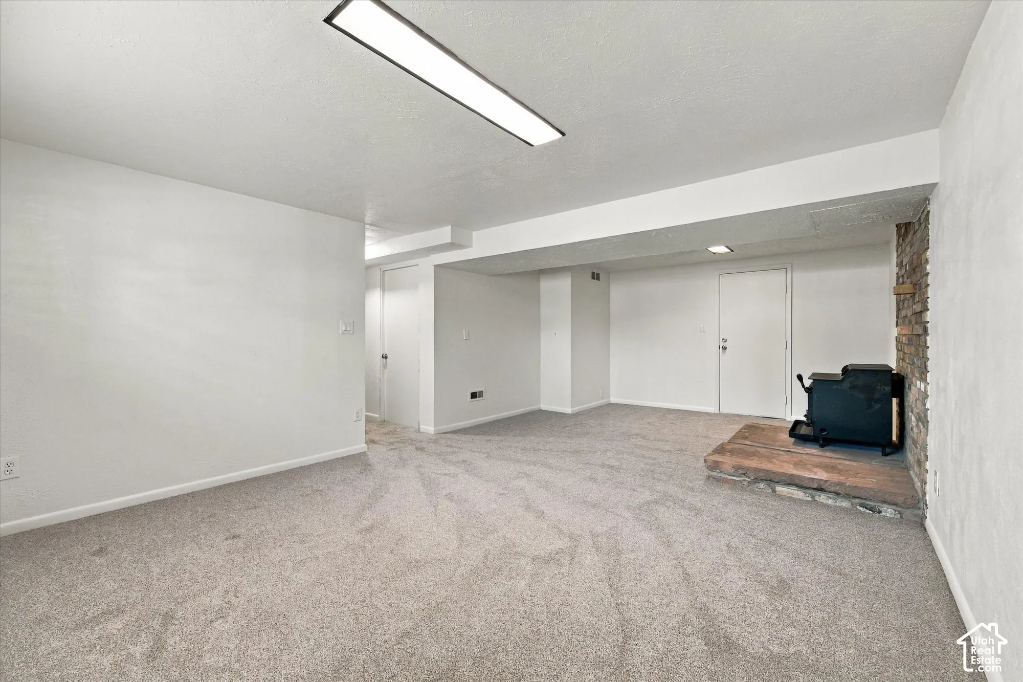 Spacious carpeted room featuring a stone-clad fireplace with a hearth, multiple entryways, and ceiling lighting