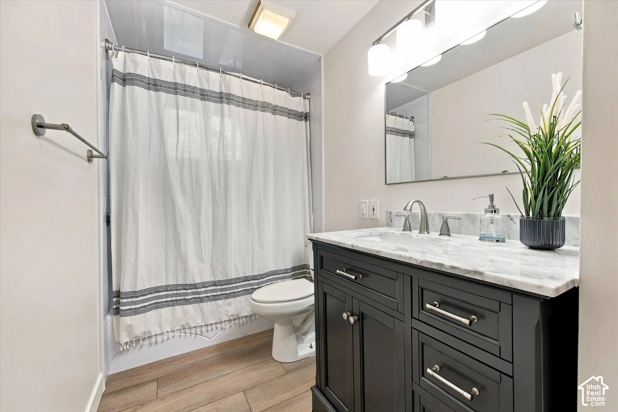 Dark wood vanity with a light-colored countertop, brushed nickel faucet, large mirror, and wood-finish flooring