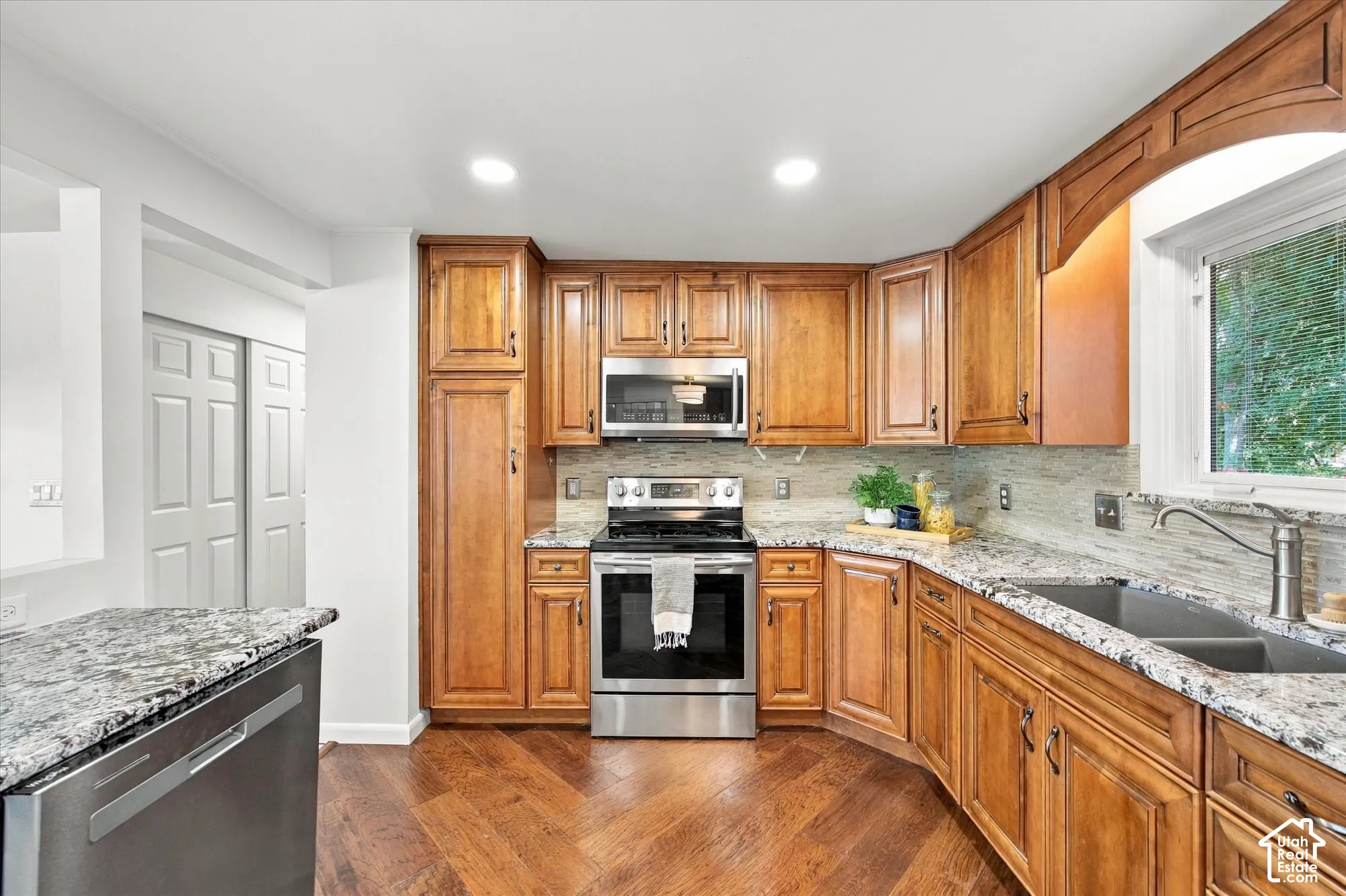 Hardwood flooring, stainless steel appliances, ample wood cabinetry, stone countertops, and a double basin sink