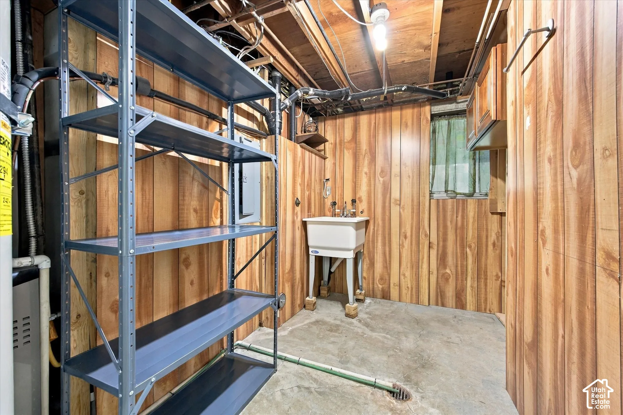 Utility sink, wood paneling, exposed ceiling joists, and concrete flooring