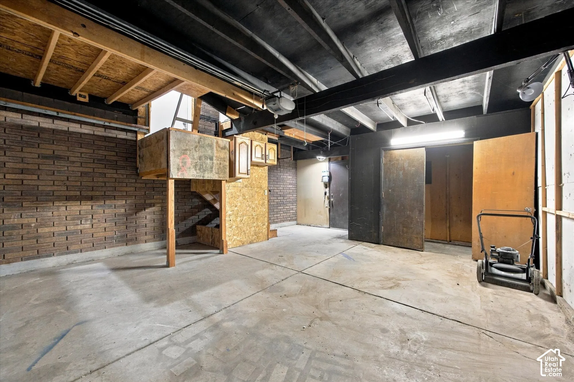 Exposed ceiling joists with painted undersides, concrete flooring, and brick-patterned wall