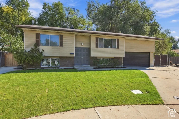 Split-level home featuring light-colored siding, dark shutters, and an attached two-car garage