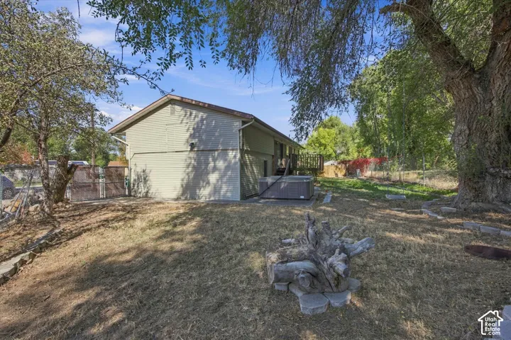 Expansive backyard featuring a hot tub, wood deck, mature trees, and a fire pit with stone surround