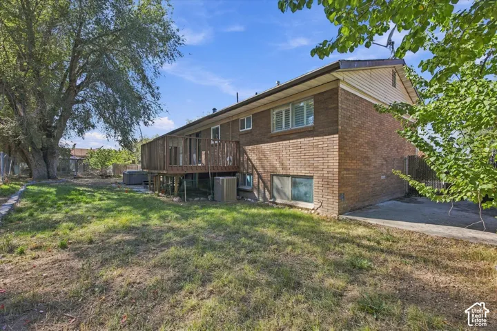 Brick exterior with a wood deck, mature trees, and a concrete patio