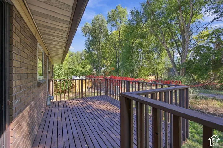 Spacious exterior deck with wood-finish railing, featuring a brick exterior and natural surroundings
