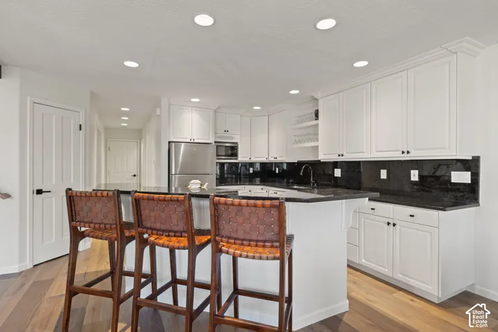 Kitchen featuring white cabinetry, dark stone countertops, stainless steel appliances, recessed lighting, and wood-finish flooring