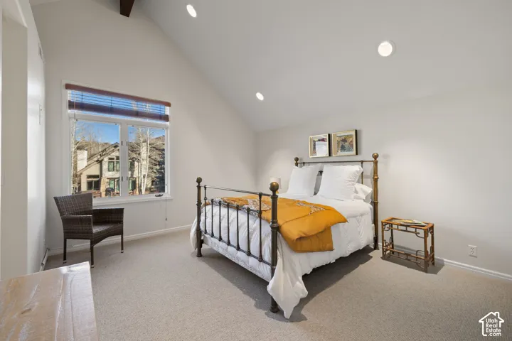 Vaulted ceiling with exposed wood beam, recessed lighting, large window, and light-toned carpeting