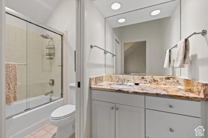 Bathroom featuring a white vanity with a natural stone countertop, undermount sink, and a mirrored wall