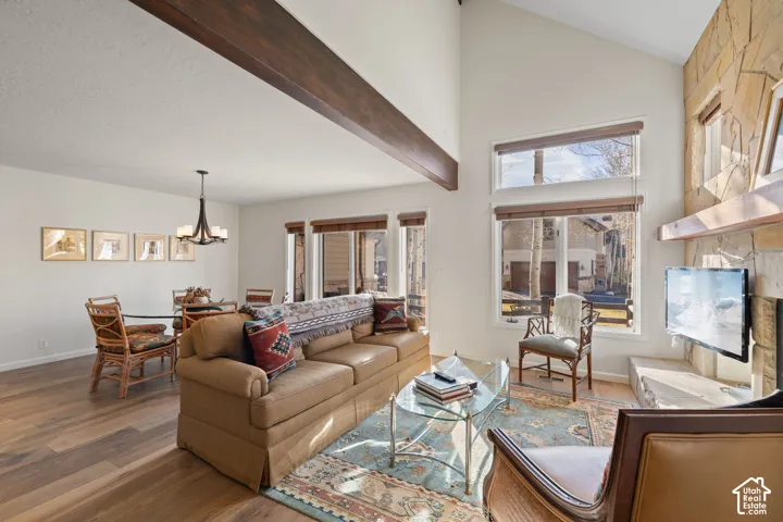 Vaulted ceiling, exposed wood beam, wood-finish flooring, stone-clad fireplace, and an integrated dining area