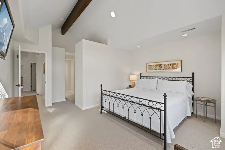 Vaulted ceiling with exposed wood beam, recessed lighting, neutral wall paint, and plush carpeting