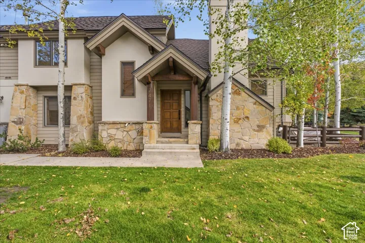 Stone veneer accents, prominent wood front door, covered entryway, gabled roofline, and mature trees