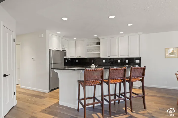 Kitchen featuring white cabinetry, dark countertops, stainless steel refrigerator, and wood-finish flooring