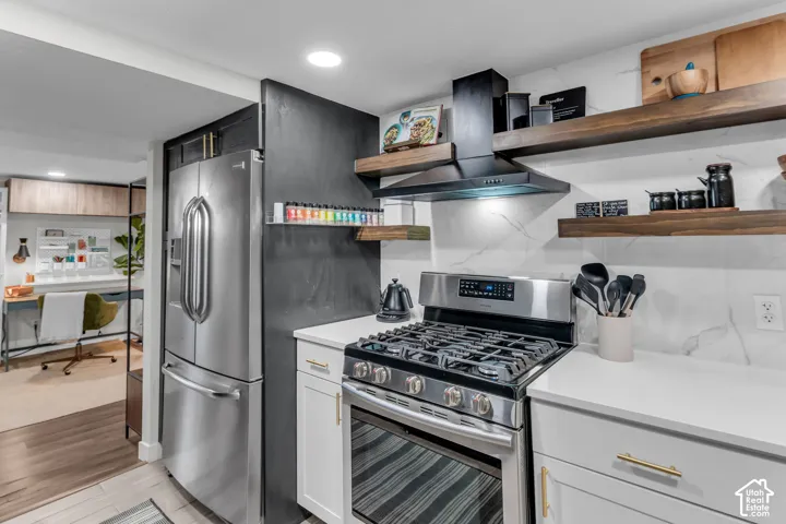 Stainless steel refrigerator, stainless steel gas range, white cabinetry with gold-tone hardware, white countertop, and wood-finish open shelving