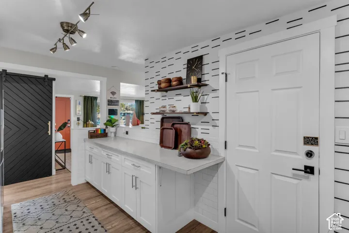 White cabinetry with brushed nickel hardware, wood-finish flooring, subway tile backsplash, track lighting, and a black barn door